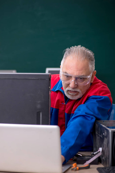 Sınıfta bilgisayar tamir eden yaşlı bir erkek tamirci. - Fotoğraf, Görsel