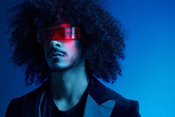 Fashion portrait of a man with curly hair on a blue background wearing red sunglasses, multinational, colored light, trendy, modern concept. High quality photo - Photo, Image