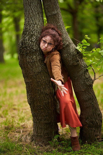 Playful mature woman in the park getting stuck between two trees - Foto, Imagem