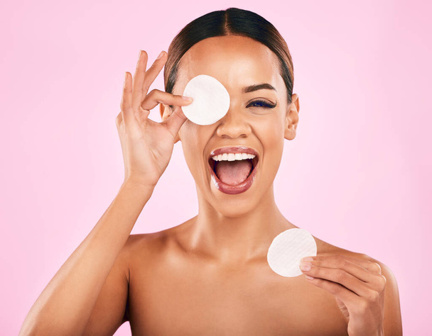 Happy woman, face and cotton pad in skincare, makeup removal or cosmetics against a pink studio background. Portrait of excited female person with cosmetic swab in beauty cleaning or facial treatment. - Photo, Image