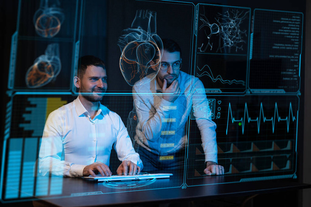 Two caucasian bearded men are looking and discussing the data on the virtual menu medical screen. Readings on the life support monitor - Zdjęcie, obraz