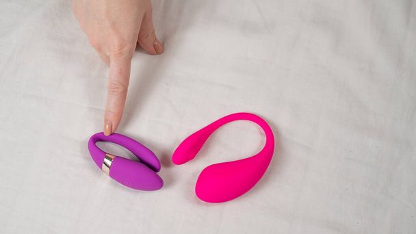 Woman choose between pink and purple vibrators while lying in bed - Фото, зображення