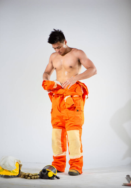 Profesionální hasič nahoře bez stál a snažil se uvázat si šaty kolem pasu na bílém pozadí. - Fotografie, Obrázek