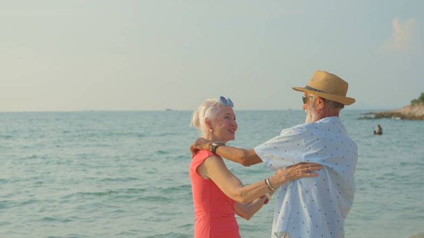 Two elderly men and women dancing at the beach on their summer vacation and they smile and enjoy their day off. - Foto, imagen