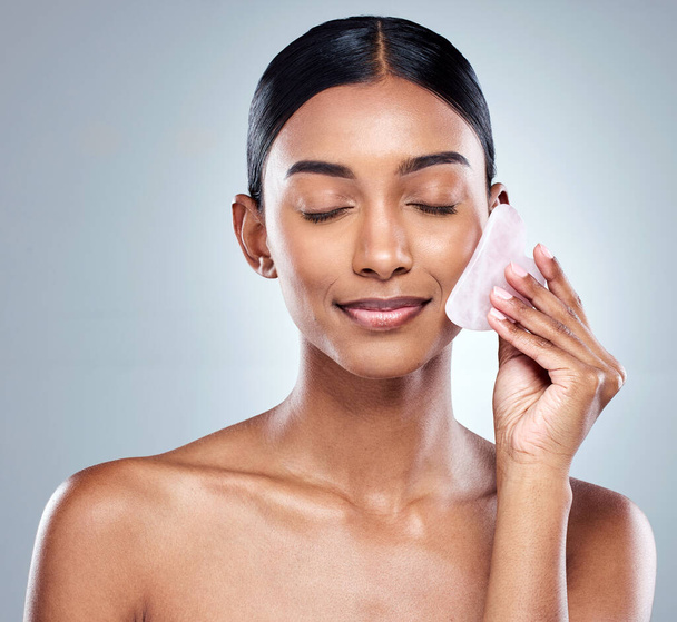 Beauty, skincare and gua sha with face of woman in studio for massage, wellness and cosmetics. Spa, self care and glow with model on grey background for facial, cosmetology and rose quartz crystal. - Foto, Imagen