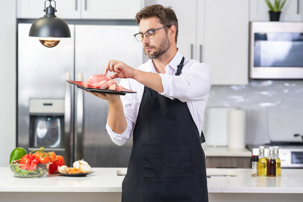 Man chef cooker hold meat beef. Male chef in chefs uniform with raw meat beef fillet. Chef man cooking raw meat beef on kitchen - Foto, Imagen
