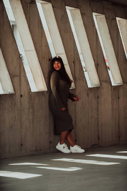 A confident and stylish plus-size woman posing by a modern building in an olive green dress, radiating beauty, empowerment, and self-love - Photo, Image