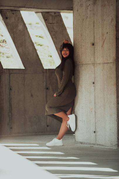 Уверенная и стильная женщина plus-size, позирующая у современного здания в оливковом зеленом платье, излучающая красоту, силу и самолюбие - Фото, изображение