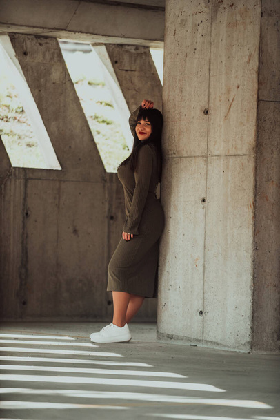Een zelfverzekerde en stijlvolle plus-size vrouw poseren door een modern gebouw in een olijfgroene jurk, stralende schoonheid, empowerment, en zelf-liefde - Foto, afbeelding