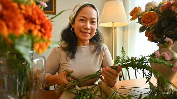 Schöne Seniorin macht einen Strauß mit frischen Blumen im Blumenladen. Konzept für Kleinunternehmen. - Foto, Bild