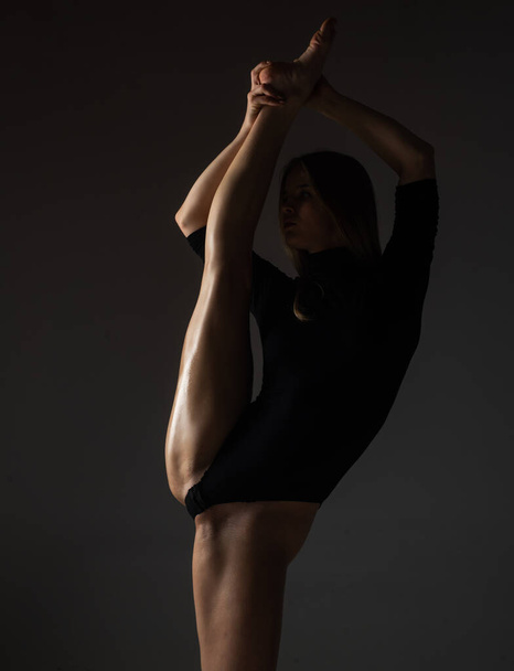 Leg-split. Sexy ballerina in black underwear stretching on black background. Concept of ballet art. Sexy pole dancer. Beautiful sexy fitness girl with great figure flexing her perfect body - Foto, Bild