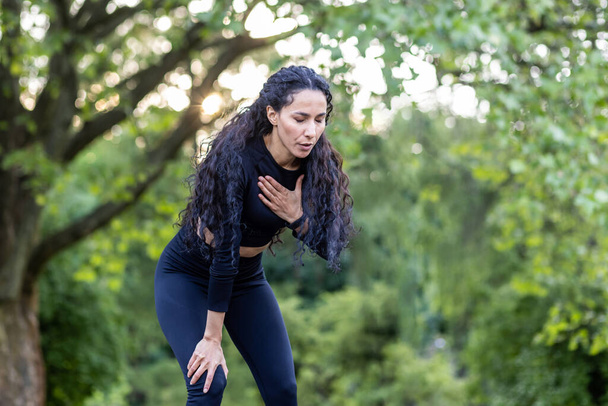 Portrait of a beautiful female athlete in the park, Hispanic woman rests and breathes during jogging and active physical exercise, female athlete in sportswear has chest pain. - Fotoğraf, Görsel