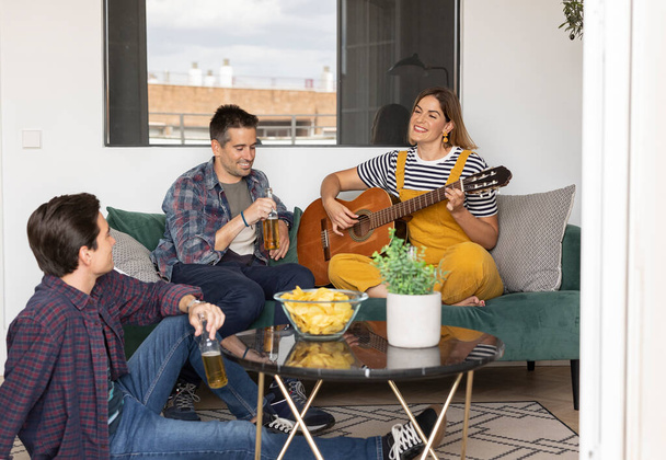 Portrait of group of young friends enjoy at home with chips beer home party, teaching to play guitar - 写真・画像