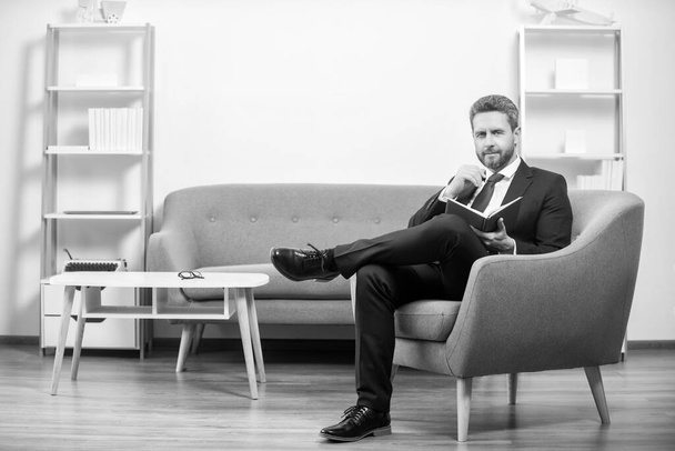 sorridente uomo d'affari maturo in abito sedersi in ufficio lettura libro. - Foto, immagini