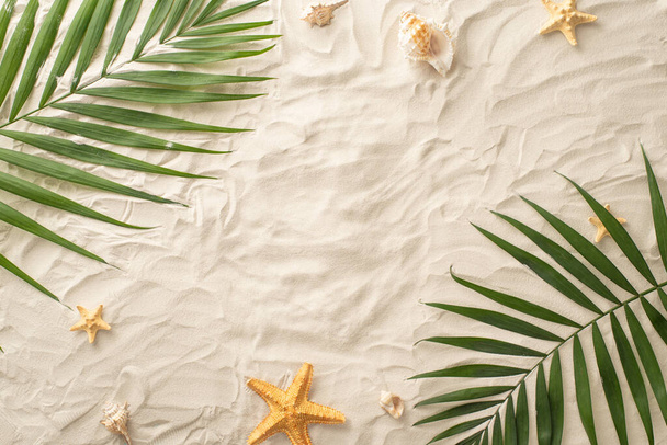 Plan your dream summer escape! Top view arrangement of accessories: seashells, starfish, and natural palm leaves. Sandy shore backdrop with a blank space for text or advertising - 写真・画像