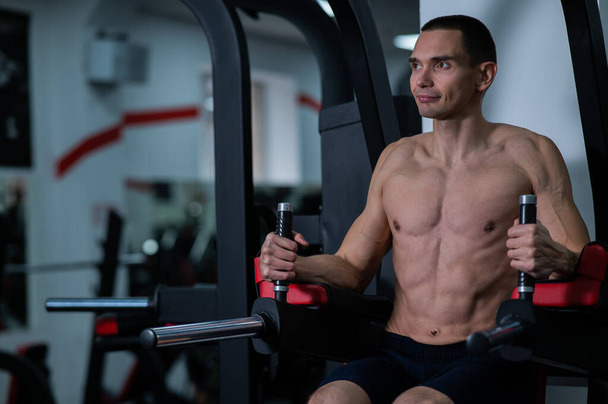 Shirtless man doing triceps dips from parallel bars in gym - Fotó, kép