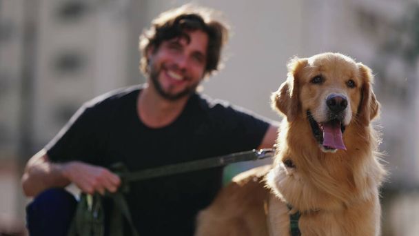 Koiranomistaja silittää kultaista noutajaansa. Kolmekymppinen mies hymyilee lemmikkikaverinsa kanssa. - Valokuva, kuva