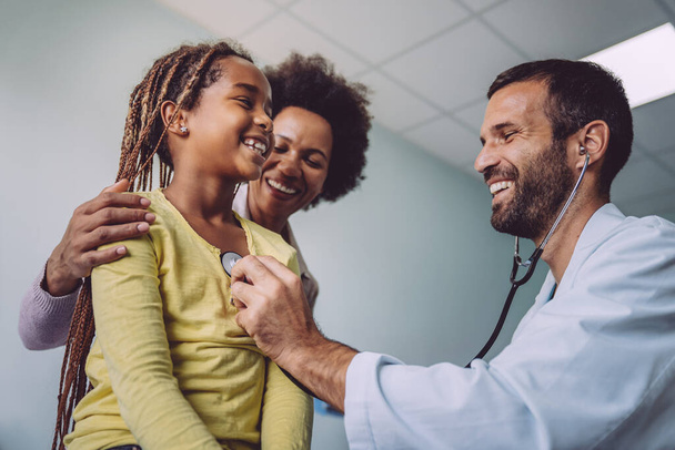 Smiling doctor examines a child with stethoscope in examination room. Healthcare medical exam people children and medicine concept - Foto, Imagen