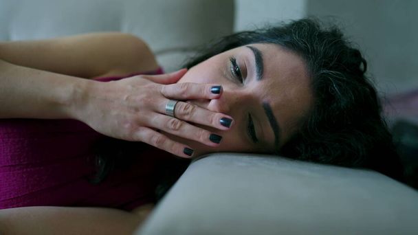 落ち込んだ女がソファに寝そべっている。感情的な苦痛に苦しむ悲しい不幸な表現で30代の女性の顔を閉じる - 写真・画像