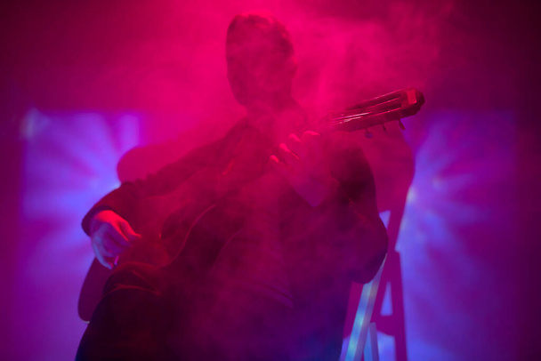 Muzikant die akoestische gitaar speelt in een mistige club met kleurrijke lichten. - Foto, afbeelding