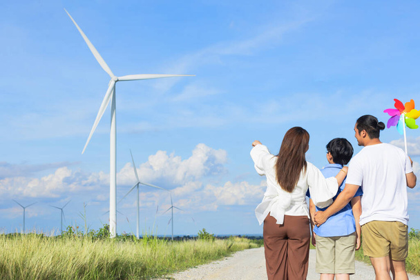 Koncepcja progresywnej szczęśliwej rodziny cieszącej się życiem na farmie turbin wiatrowych. Generator energii elektrycznej z generatora turbin wiatrowych po stronie wsi ze wzgórzem i górą na horyzoncie. - Zdjęcie, obraz
