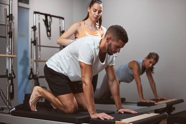 Jeunes femmes et homme faisant de l'exercice dans une salle de gym avec entraîneur personnel. - Photo, image