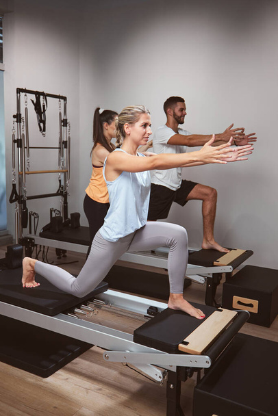 Young woman and man exercising in a gym with personal trainer on pilates machine. - Foto, immagini