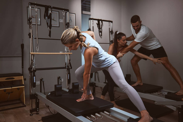 Młoda kobieta i mężczyzna ćwiczący na siłowni z osobistym trenerem na pilates machine. - Zdjęcie, obraz
