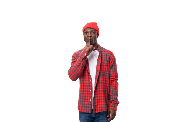 handsome joyful dark-skinned man in a casual plaid shirt keeps a secret on a white background with copy space. - Photo, Image