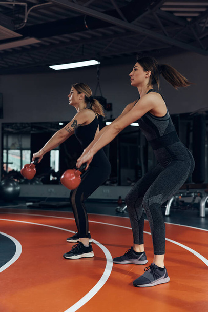 Спортивные женщины, делающие русские гиревые упражнения в спортзале. - Фото, изображение