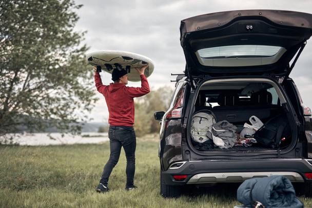 Windsurfer e campista desempacotando equipamentos de um carro na natureza perto da costa do lago. - Foto, Imagem