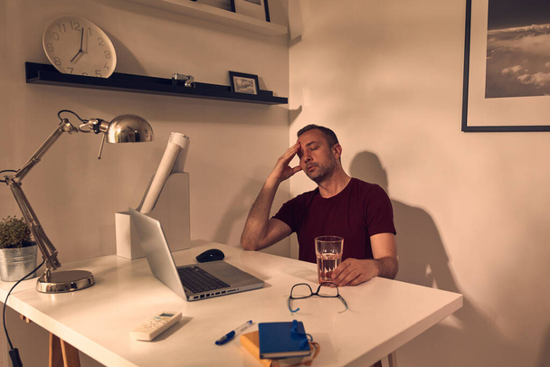 Человек с головной болью и чувство усталости во время работы на ноутбуке дома. - Фото, изображение