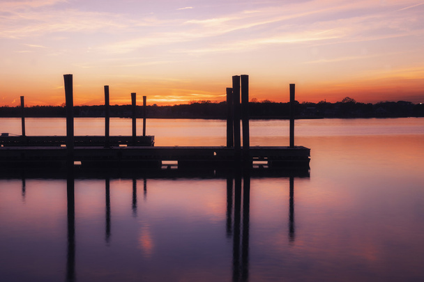 Dock vazio na água sob um pôr-do-sol rosa e laranja
 - Foto, Imagem