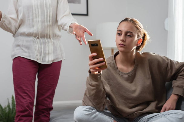 Madre teniendo problemas con una adolescente perezosa en casa mientras juega videojuegos en un teléfono inteligente. - Foto, Imagen