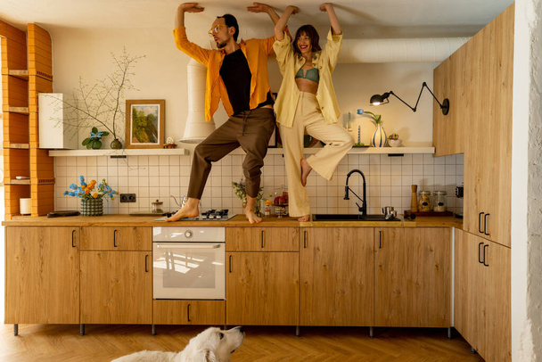 Young couple having fun, standing together on a kitchen table at their stylish and cozy apatment studio. Man and woman spends leisure time happily indoors - Valokuva, kuva