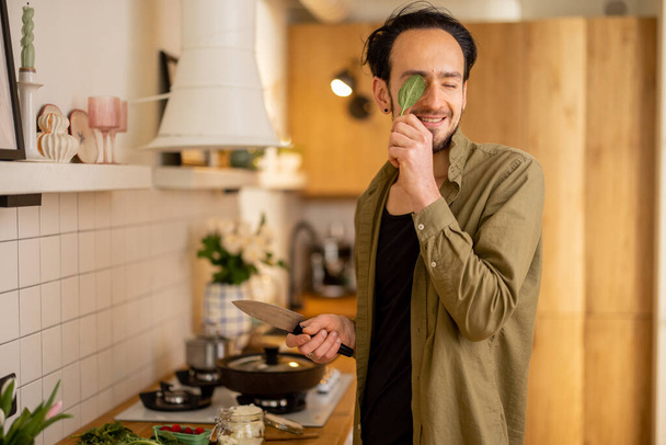 Mies pitää hauskaa, kun ruoanlaitto terveellistä kasvisruokaa pinaatti lehdet keittiössä kotona. Terveiden kotimaisten elämäntapojen käsite - Valokuva, kuva