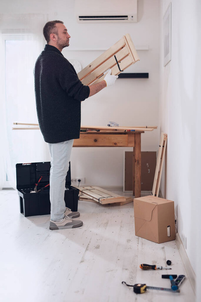 Hombre montando nuevos estantes de madera y muebles en el apartamento. - Foto, Imagen