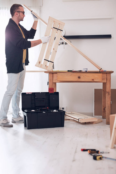 Mann baut neues Holzregal und Möbel in der Wohnung zusammen. - Foto, Bild