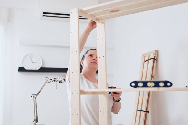 Woman assembling new wooden shelf and furniture in the apartment. - Photo, Image
