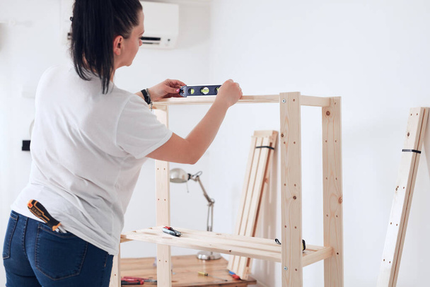 Mujer montando nuevos estantes de madera y muebles en el apartamento. - Foto, imagen