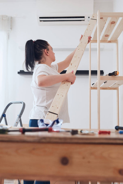 Mulher montando nova prateleira de madeira e móveis no apartamento. - Foto, Imagem