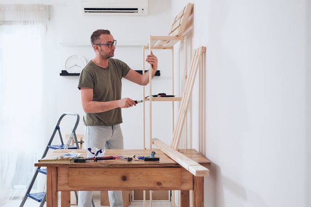 Muž montáž nové dřevěné police a nábytek v bytě. - Fotografie, Obrázek