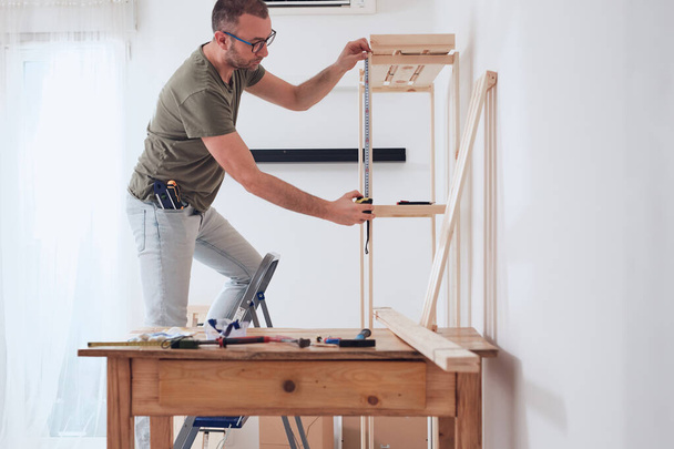 Άνδρας συναρμολόγηση νέων ξύλινων ραφιών και επίπλων στο διαμέρισμα. - Φωτογραφία, εικόνα