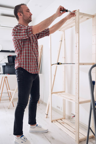 Man assembling new wooden shelf and furniture in the apartment. - Photo, Image