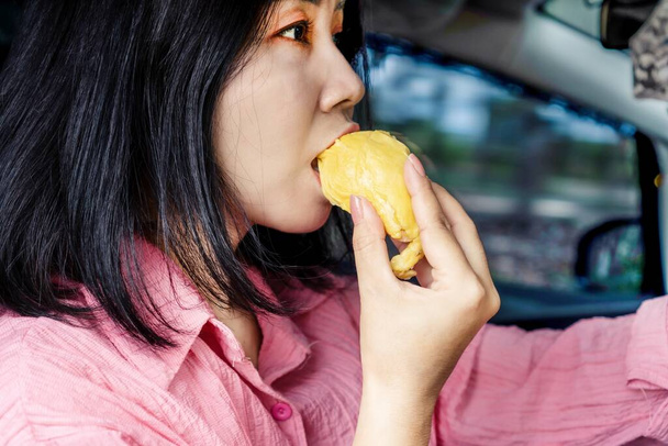 Mujer asiática comiendo fruta durian mientras conduce, hacer fuerte olor en el coche - Foto, Imagen