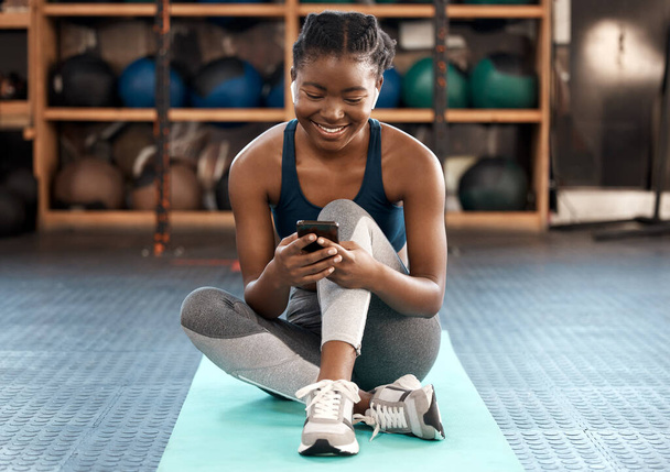 Happy black woman, fitness and phone for social media, communication or networking at the gym. African female person or athlete typing, texting or chatting on mobile smartphone after workout exercise. - Photo, image