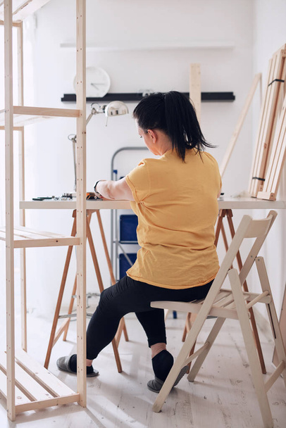 Vrouw monteert nieuwe houten plank en meubels in het appartement. - Foto, afbeelding