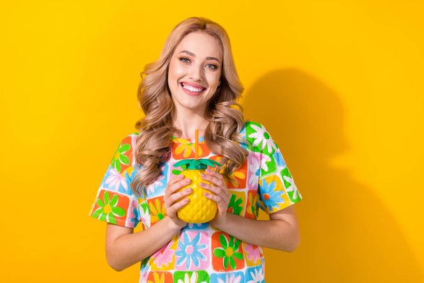 Photo of satisfied pleasant girl with wavy hairdo dressed colorful t-shirt hold pineapple cup cocktail isolated on yellow color background. - 写真・画像