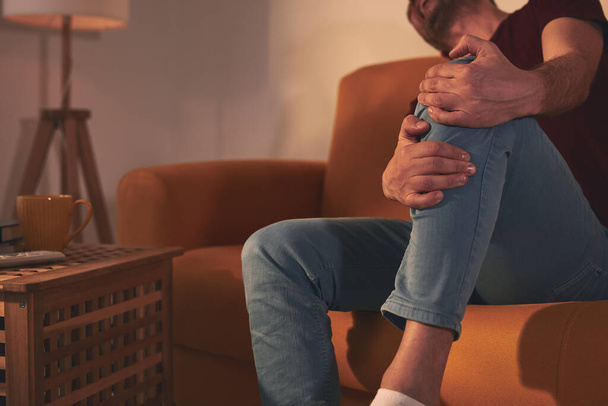 Homem com dor no joelho sentado em um sofá em casa. - Foto, Imagem