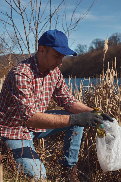 Vapaaehtoinen ja ympäristöaktivisti siivoamassa likainen järvi rannalla täynnä roskia. - Valokuva, kuva